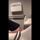 A hidden camera records an unsuspecting girl from behind as she sits on a toilet in a public restroom and takes a shit. You can see her seated rear view throughout, and bathroom audio is audible. Vertical format video. About 2.5 minutes.
